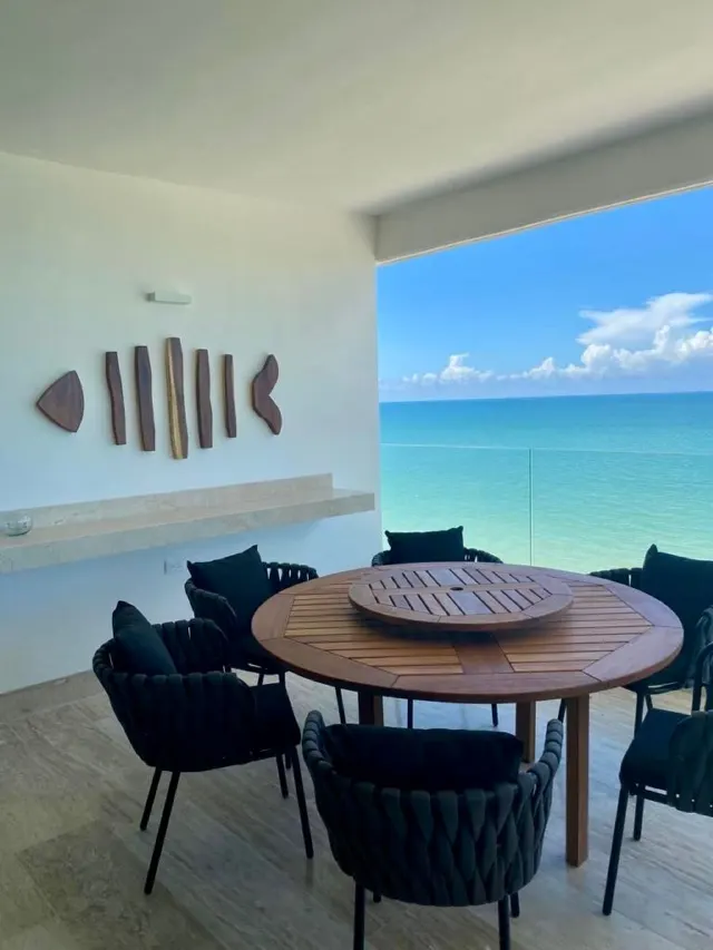 Terraza con comedor de madera frente al mar turquesa