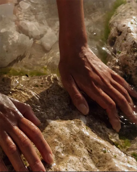 Manos acariciando una roca bajo el agua clara