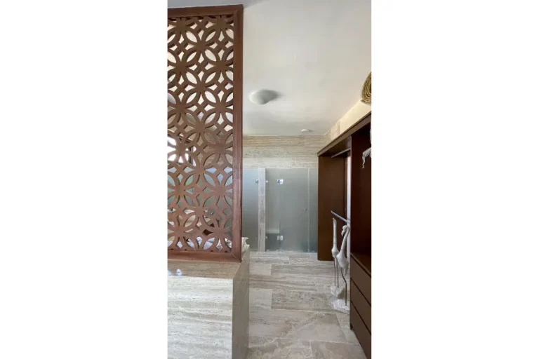 Baño con celosía de madera, piso y muros de piedra, ducha con cancel de cristal y mueble abierto de madera.