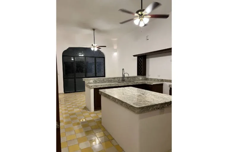 Cocina con cubiertas de piedra moteada, barra, fregadero, ventiladores de techo y piso de cuadros amarillos y blancos.