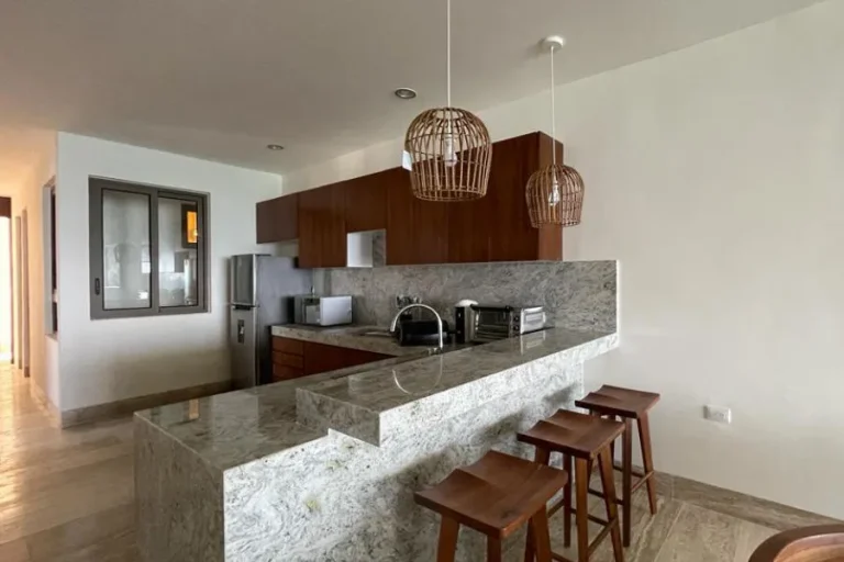 Cocina con gabinetes de madera, barra de piedra, tres bancos y dos lámparas colgantes de fibras naturales.