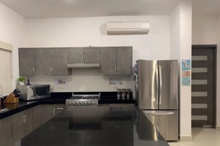 Cocina con gabinetes grises, isla de cubierta negra, estufa, microondas, refrigerador y aire acondicionado.