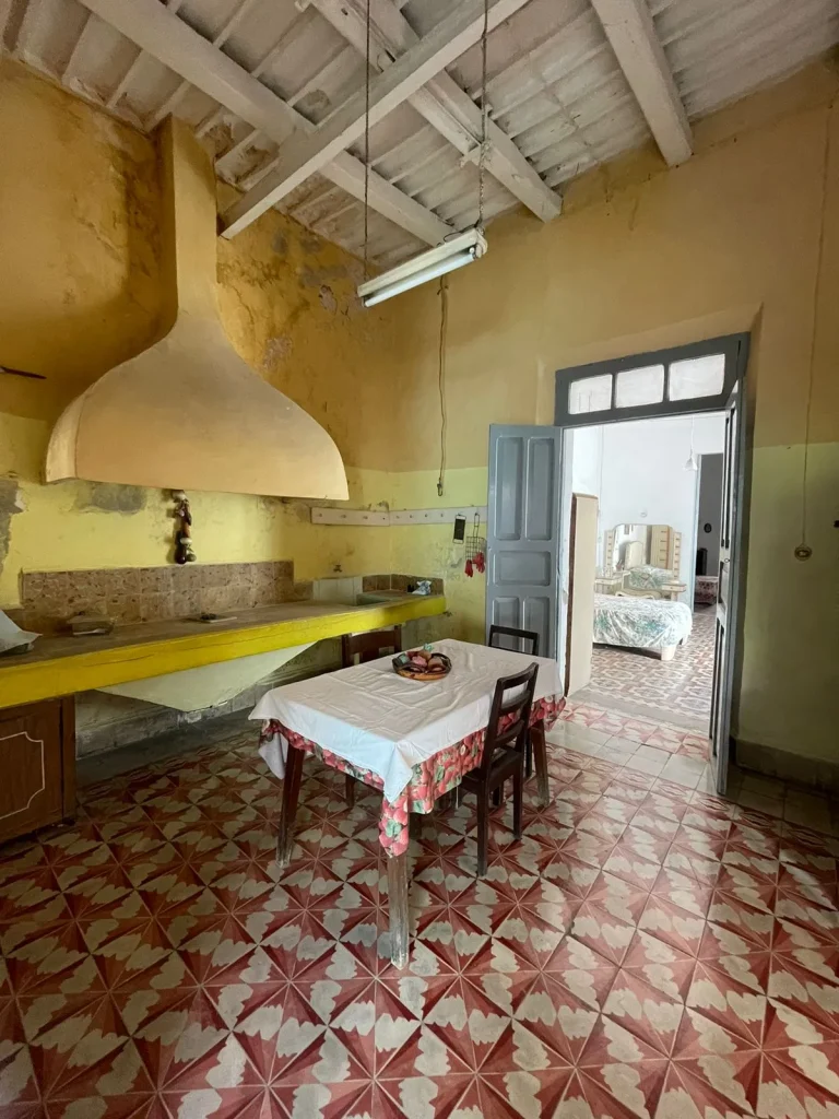 Cocina de paredes amarillas con campana amplia, mesa con mantel, vigas blancas y piso de mosaico rojo y blanco.