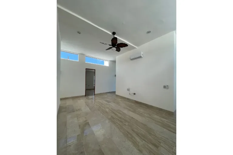 Estancia vacía con piso brillante, ventanas altas, ventilador de techo y aire acondicionado en la pared.