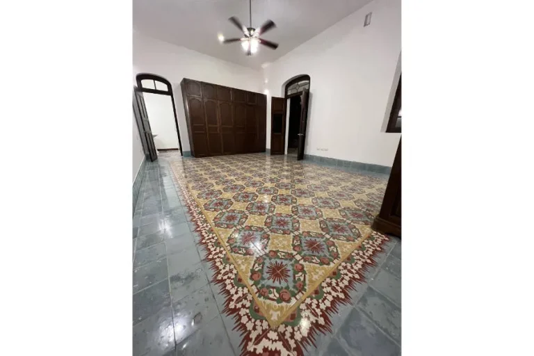 Habitación con piso de mosaicos multicolores, armario de madera, puertas altas y ventilador de techo.