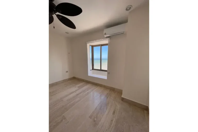 Habitación vacía con piso de piedra clara, ventana con vista al mar, aire acondicionado y ventilador de techo.