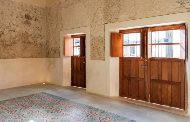 Habitación con muros de textura rugosa, puertas de madera con ventanas y una sección de piso con motivos de colores.