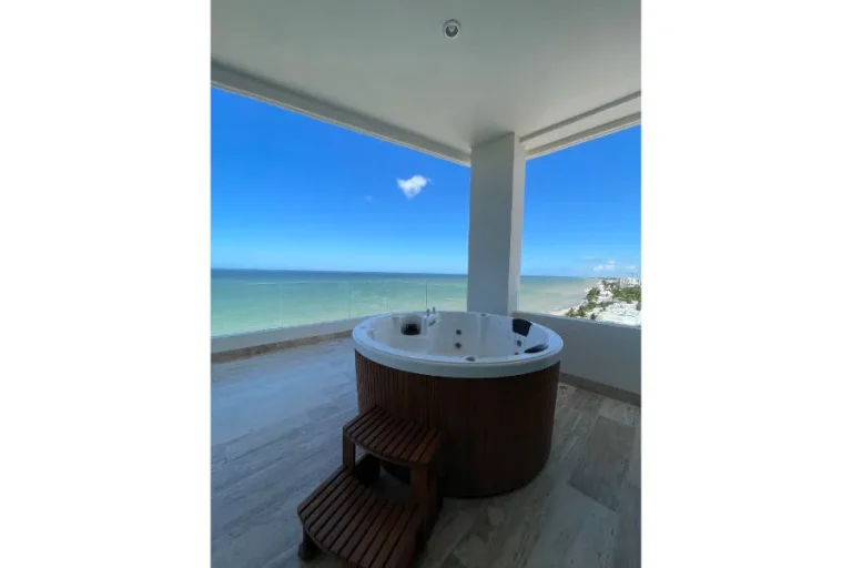 Jacuzzi circular con revestimiento de madera y escalones en una terraza techada con vista al mar.