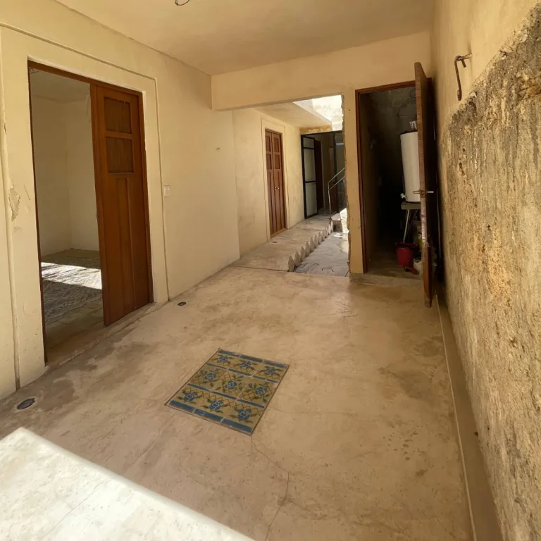 Pasillo con puertas de madera, piso de concreto con un detalle de mosaico y muro lateral de acabado rugoso.