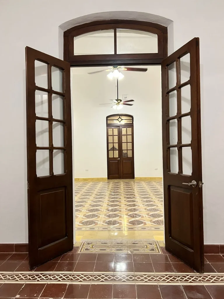 Puertas dobles de madera abiertas hacia una estancia con pisos de mosaico y ventiladores de techo.