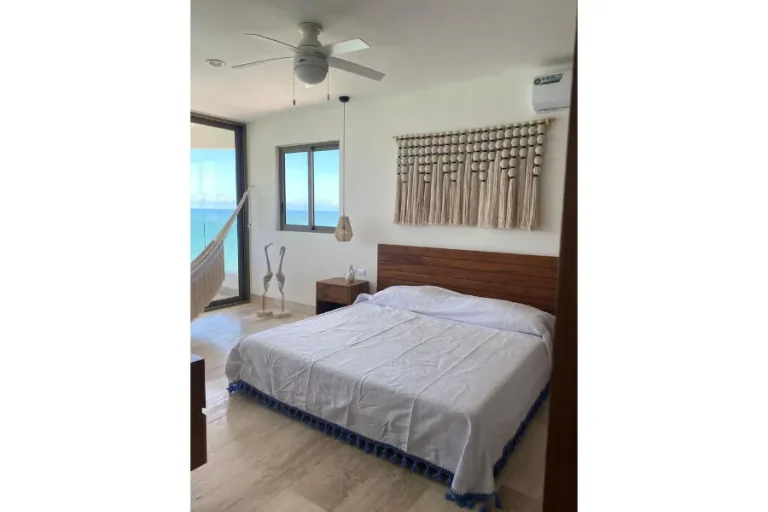 Recámara con cama de cabecera de madera, tapiz de macramé, hamaca junto al ventanal y vista al mar.