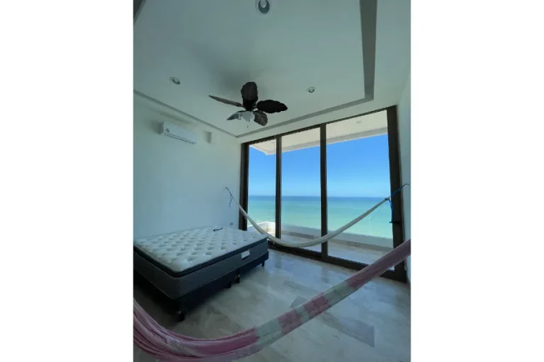 Recámara con colchón sin vestir, dos hamacas, ventilador de techo y puertas de cristal con vista al mar.