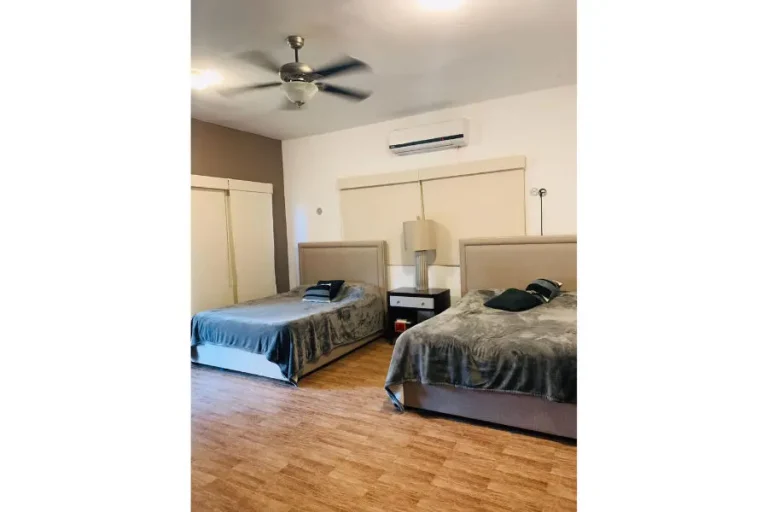 Recámara con dos camas, cabeceras tapizadas, buró central, aire acondicionado y ventilador de techo.