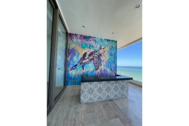 Terraza techada con barra revestida de azulejos, mural de una tortuga y vista al mar.
